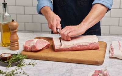 Raw boneless pork loin being sliced on a wooden cutting board.
