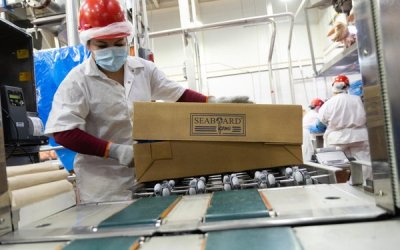 Worker in hard hat handling Seaboard Farms boxes inside pork processing facility.